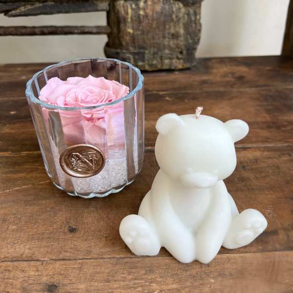 Pink rose in a clear glass holder beside a white bear-shaped candle