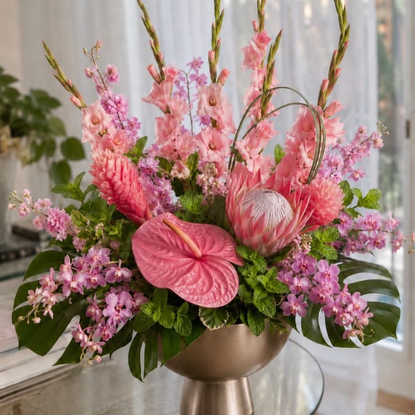 Pink tropical floral arrangement in a gold pedestal vase