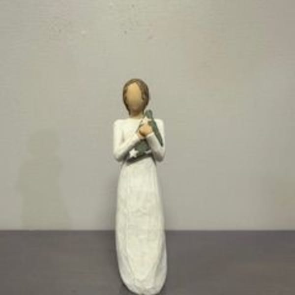 A small angel figurine in a long white dress holding a dove