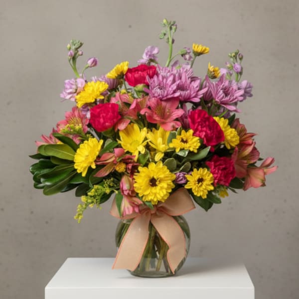 Mixed bouquet of pink, yellow, and purple flowers in a glass vase with a ribbon