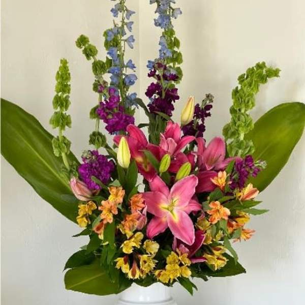 Tall mixed bouquet of lilies and purple flowers in a white pedestal vase