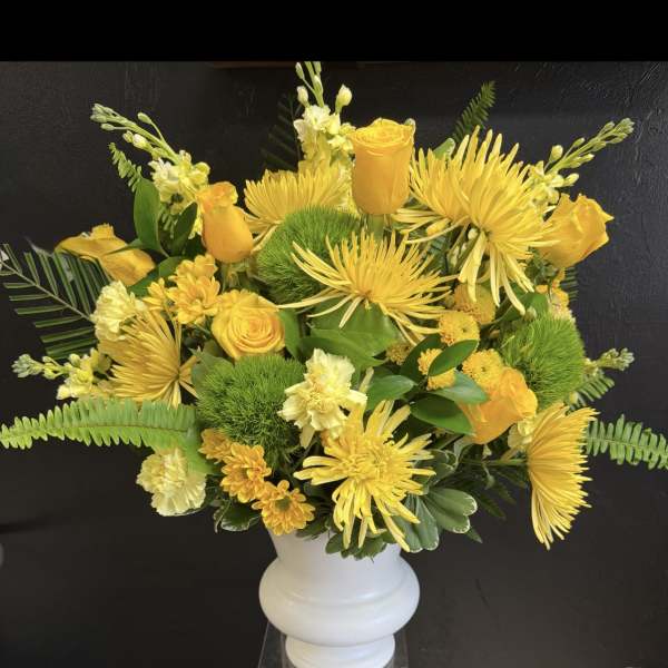 Yellow floral arrangement in a white vase with roses and spider mums