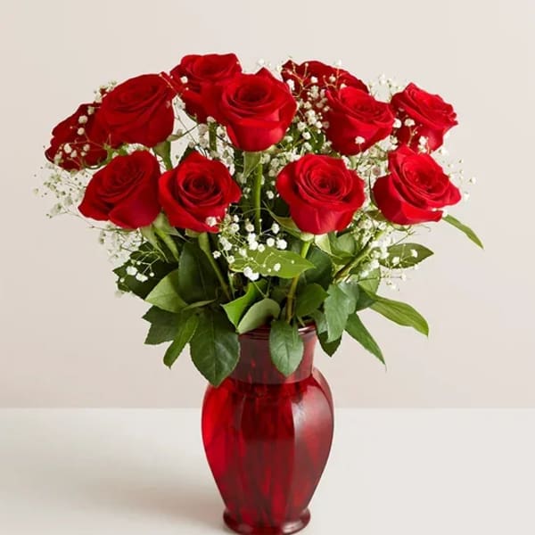 Red roses arranged in a red glass vase with baby's breath