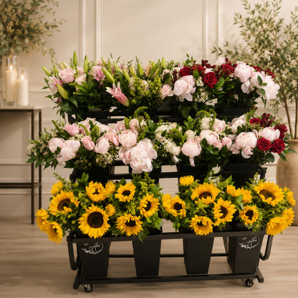 Tiered flower display with sunflowers, pink lilies, and roses in black containers