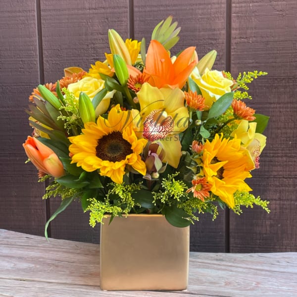 Bright mixed bouquet with sunflowers, lilies, and roses in a gold vase
