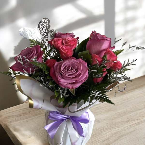 Bouquet of pink and purple roses wrapped in white paper with a lavender ribbon