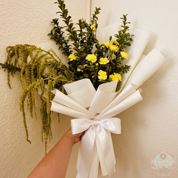 Handheld bouquet with yellow flowers, greenery, and white wrapping tied with a satin bow