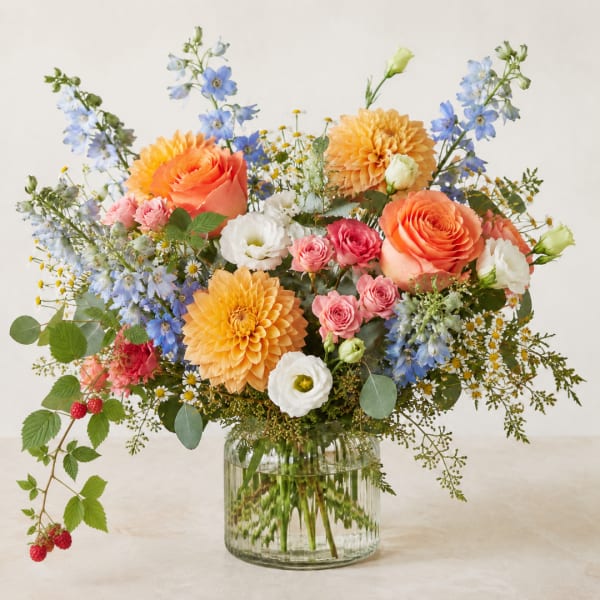 Mixed bouquet of orange, pink, blue, and white flowers in a glass vase