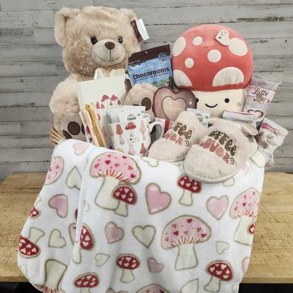 Gift basket with a teddy bear, mushroom plush, snacks, and a heart-patterned blanket