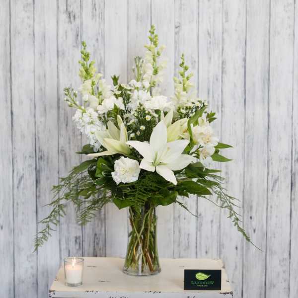 White lilies and snapdragons in a clear glass vase with a lit candle nearby