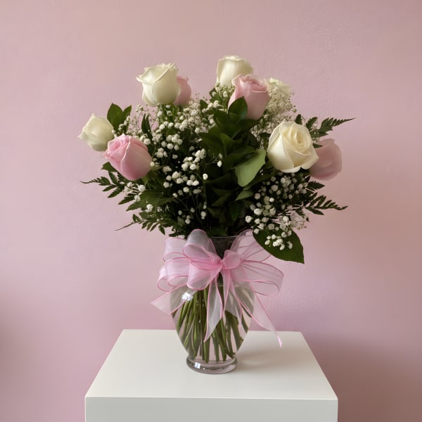 Pink and white roses in a glass vase with a pink ribbon