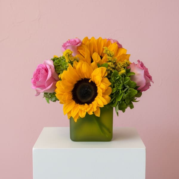 Sunflowers and pink roses arranged in a green square vase