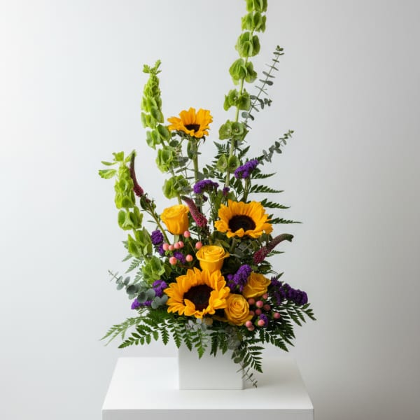 Tall floral arrangement with sunflowers and yellow roses in a white box vase