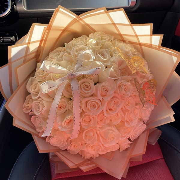 Large bouquet of pale pink roses wrapped in peach paper with a ribbon