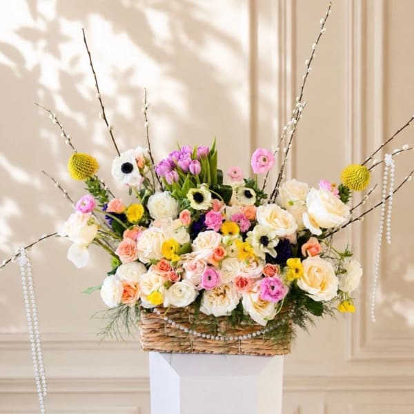 Mixed bouquet of roses, ranunculus, and tulips in a woven basket with tall branches