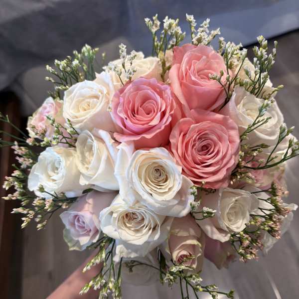 Handheld bouquet of pink and white roses with small filler flowers