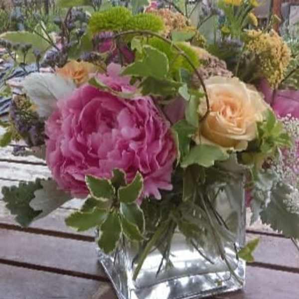 Pink and peach roses in a square glass vase with greenery