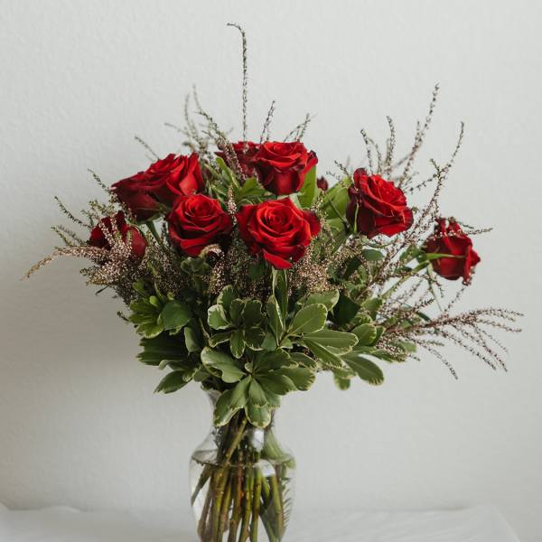 Red roses arranged in a clear glass vase with greenery