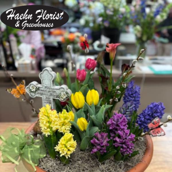 Mixed spring flowers in a shallow terracotta bowl with a decorative cross