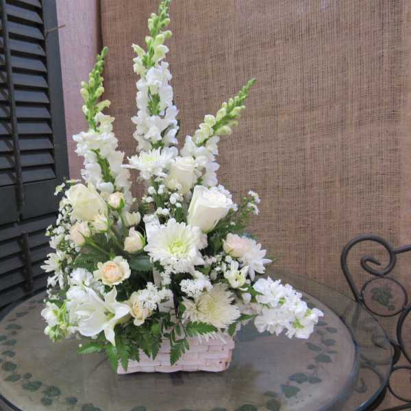 White floral arrangement in a pale basket on a glass table