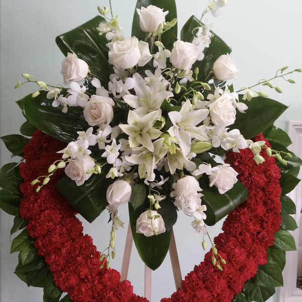 Heart-shaped floral wreath with white roses and lilies on a stand