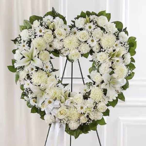 Heart-shaped white floral wreath on a black stand with a white ribbon