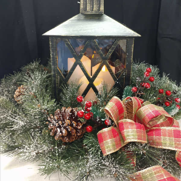 Holiday lantern centerpiece with pinecones, berries, and a plaid ribbon