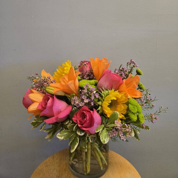 Bright mixed bouquet of roses, lilies, and sunflowers in a glass vase