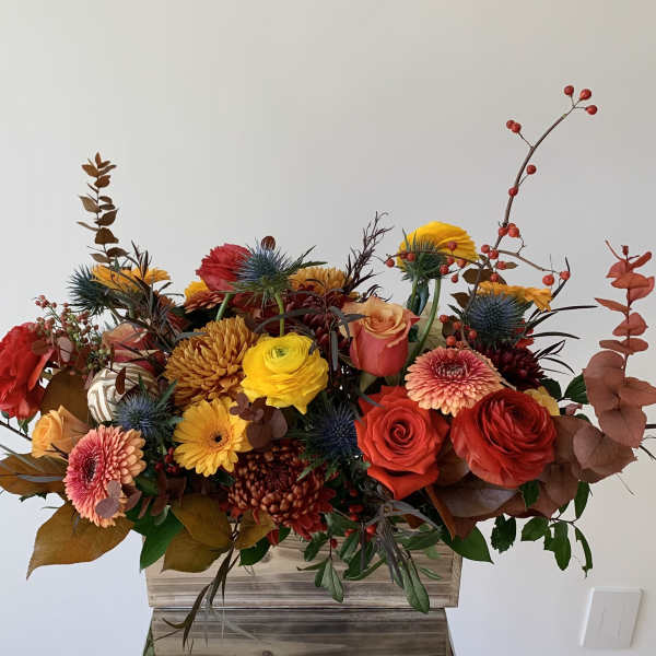 Mixed bouquet of red, yellow, and peach flowers in a wooden container