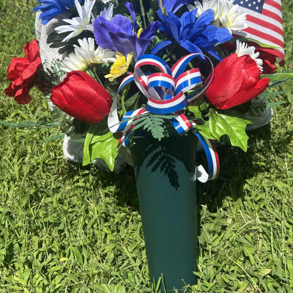 Red, white, and blue floral arrangement in a green vase with an American flag ribbon