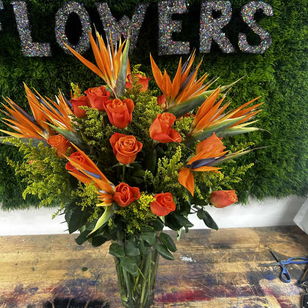 Orange roses and bird of paradise in a glass vase