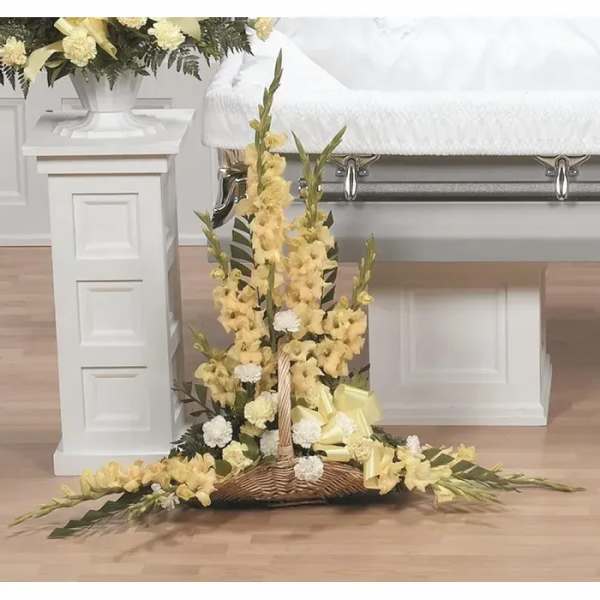 Yellow floral funeral spray on a wicker base beside a casket