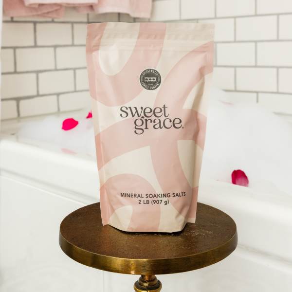 A pink and cream pouch of mineral soaking salts on a round stand.