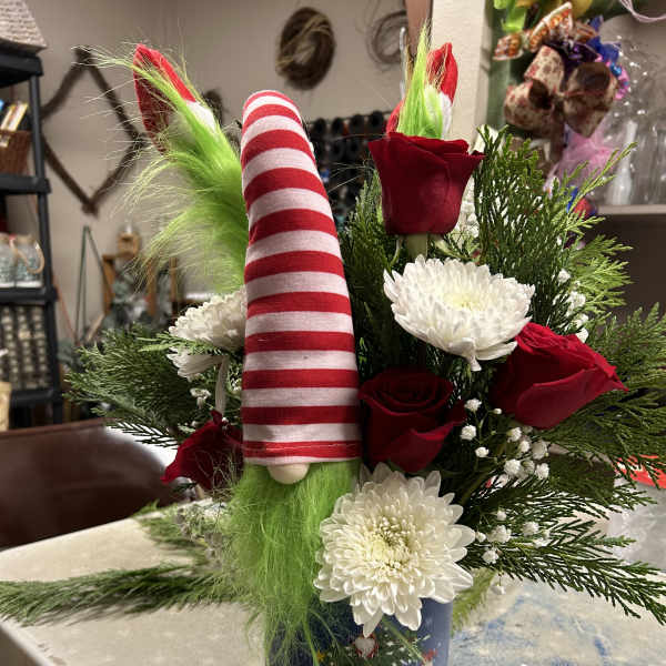 Christmas arrangement with red roses, white mums, and a striped gnome in a holiday tin