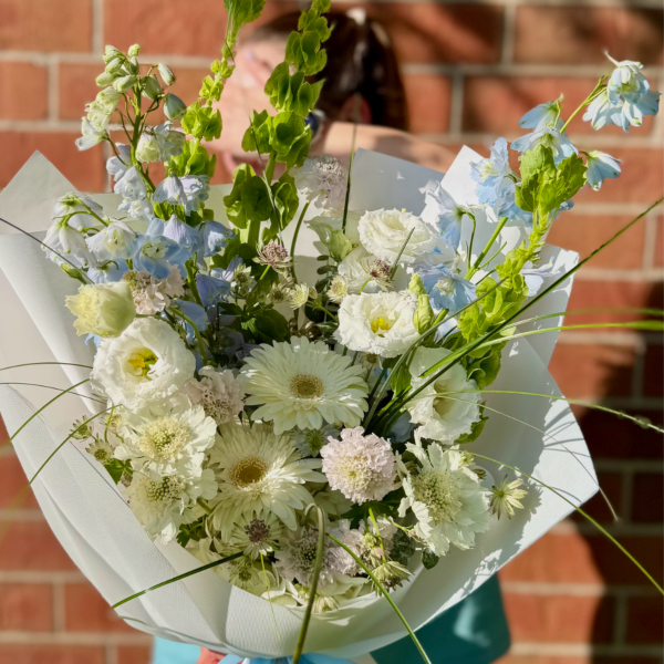Bouquet of white and pale blue flowers wrapped in white paper with a blue ribbon