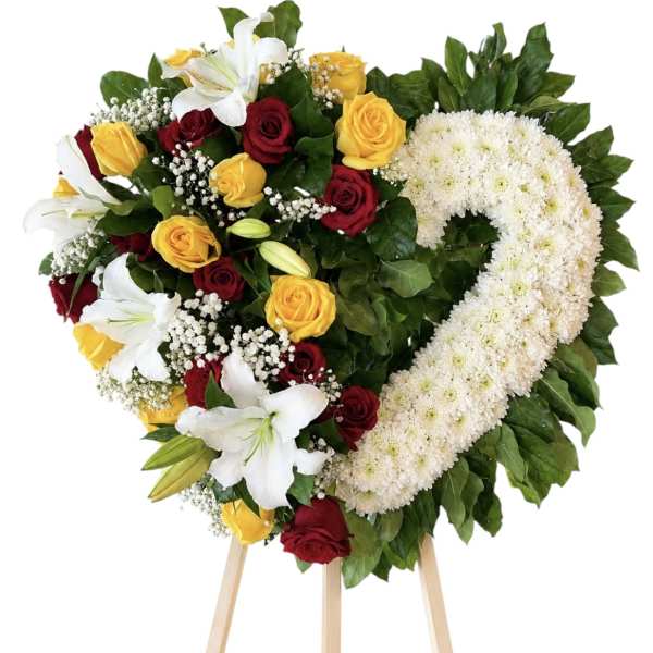 Heart-shaped floral wreath with red and yellow roses, white lilies, and white chrysanthemums on an easel