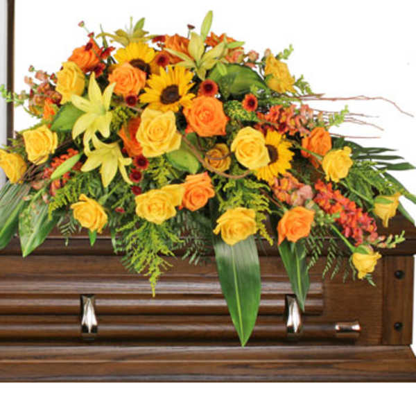 Yellow and orange casket spray of roses, lilies, and sunflowers on a wooden casket.