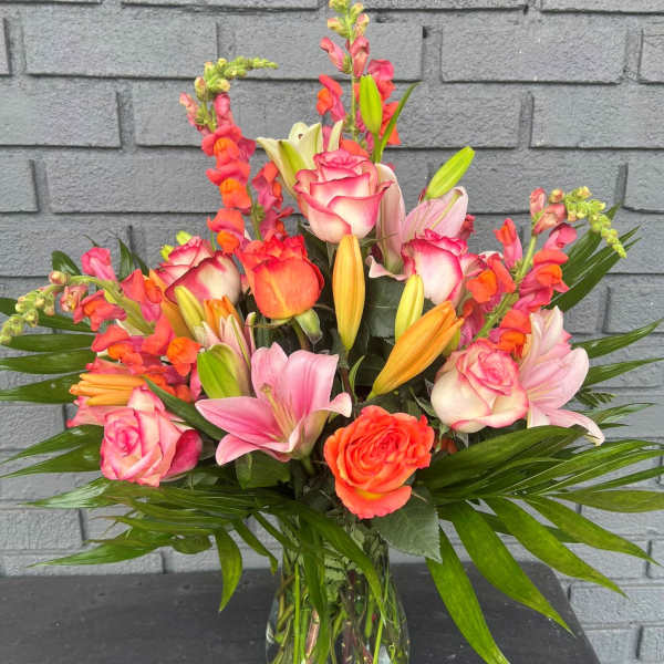 Mixed bouquet of pink roses, lilies, and orange snapdragons in a glass vase