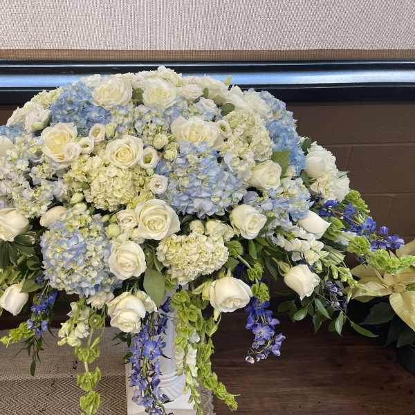 Large white and blue floral arrangement in a white pedestal vase