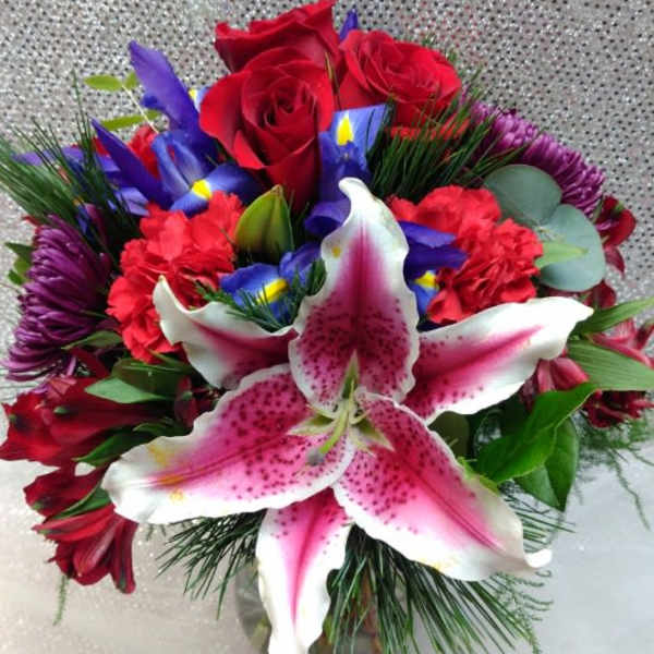 Bouquet of red roses, pink lilies, and purple flowers in a glass vase