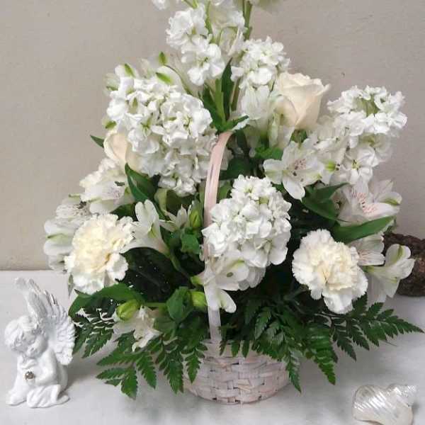 White floral arrangement in a woven basket with a pink ribbon handle