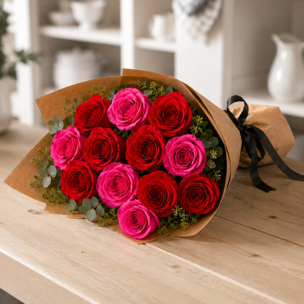 Bouquet of red and pink roses wrapped in brown paper with a black ribbon