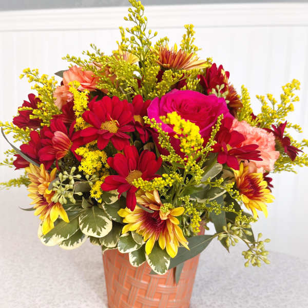 Mixed bouquet of red, pink, and yellow flowers in a peach basket vase