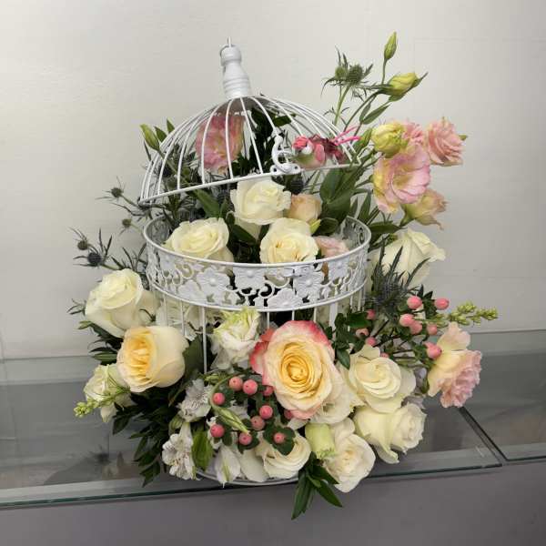 White roses and pink lisianthus arranged in a decorative white birdcage.