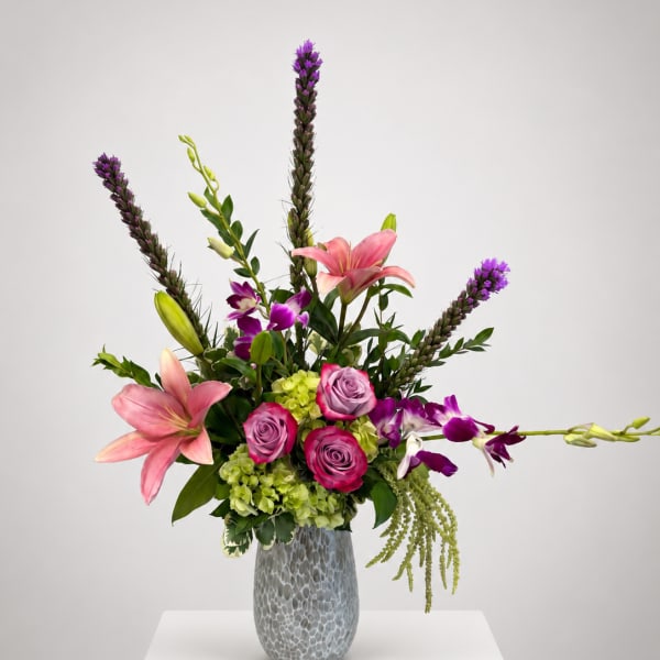 Pink lilies and roses in a gray vase with purple orchids