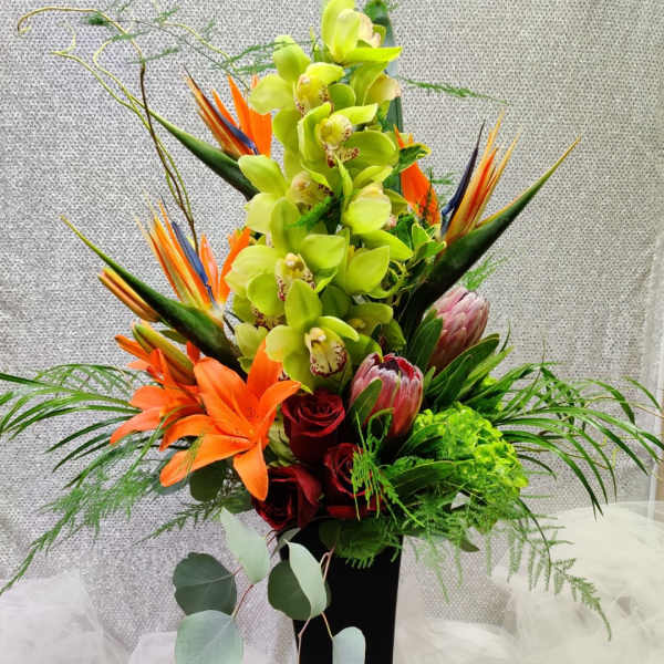 Tall tropical bouquet with green orchids, orange lilies, and red roses in a black vase