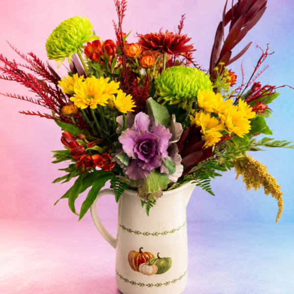 Mixed bouquet in a white ceramic pitcher with yellow, green, purple, and red flowers.