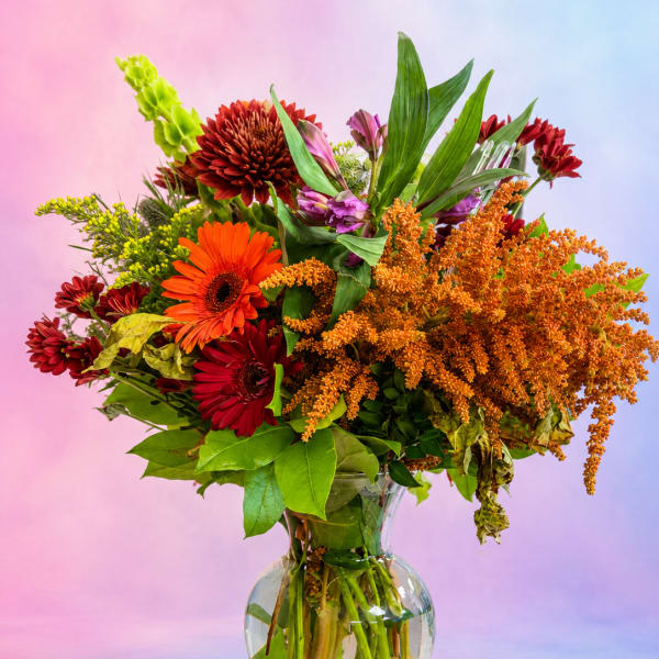 Mixed bouquet of orange, red, and purple flowers in a clear glass vase