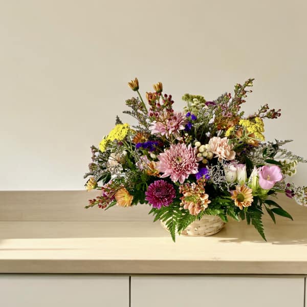 Mixed bouquet in a woven basket with pink, yellow, and purple flowers