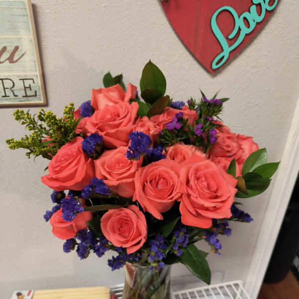 Bouquet of coral roses and purple filler flowers in a glass vase